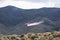 Small red and white plane just beginning to drop fire retardant on a fire below power lines in the desert