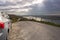 Small rented car parked off road on top of a hill with beautiful view on ocean and mountain landscape. Sky road, Clifden, county