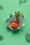 Small ripe orange pineapple cradled in human hand. Hand with the fruit show out of torn paper hole. Tropical neo mint green