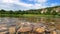 A small river in a beautiful area. Rocky mountains overgrown with shrubs in the background. Many stones of different