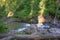 A small river flowing through the morning forest in a rocky channel forming rapids