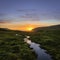 Small River Guiding the way to Sunset with Red Clouds and Blue Sky. (Faroe islands)