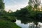 A small river between steep banks with bushes and grass