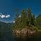 Small rocky islet overgrown with trees near the shore of the lake against the blue sky