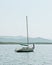 Small sailing boat on calm sea with hills