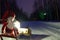 Small santa travelling home on kicksled on snowy road with suitcase and lantern