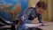 A small school girl draws in a notebook standing near the desk at school.