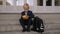 A small schoolboy boy sits on the steps of the school and opens a lunch box.