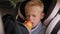 Small schoolboy boy is sitting in a car seat with a backpack and eating an apple