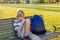 Small schoolboy sitting on bench at schoolyard with backpack, writing in notebook after school or during recess