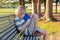 Small schoolboy sitting on bench at schoolyard with backpack, writing in notebook after school or during recess