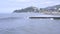 Small sea waves with foam break on breakwater. Aerial view resort town, mountains in background. Beach season. Sea coast landscape