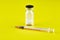 Small sealed bottle with medicine and syringe on yellow background