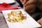 A small serving of lasagne on a square plate, person holds a fork in hand and eats