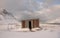 Small shack house surrounded by snowy mountains under a cloudy sky