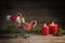 Small shopping cart with presents, christmas decoration, sweets and Santa hat on a rustic wooden table with burning candles and