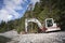 Small shovel digger standing on gravel next to lake and forest