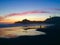 Small silhouetted boy playing in pacific ocean tide, reflecting blue,pink, orange sunset sky