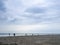 Small silhouettes of people on the shore. People in the distance stand and look at the sea. Overcast weather