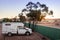 Small sized 4wd campervan parked on a camping site in the middle of the desert. Sunset time. Green fence and tree next to the car