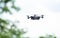 Small Smart Drone quadrocopter Flying on White Sky and Green trees.