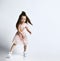 Small smiling cute girl in casual summer dress and sneakers moving in action over white wall background