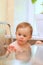 Small smiling white child sitting on a chair at the glass table in the kitchen near the window. The image is reflected from the