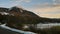 A small snow capped mountain, by a frozen lake