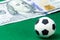 A small soccer ball on a green background next to a hundred-dollar bill. Concept money and sports, betting on football. Macro. Sup