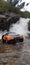 Small sports toy car parked atop a large, craggy rock formation, against a waterfall