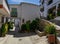 A small square in Berchules with a stone fountain, a tinao, white houses, a sloping street and abundant flower pots