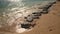 Small stones visible at sand beach washed by sea water on a sunny day, closeup detail.