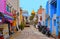 Small street with old colorful buildings, motorcycles and cars with chaotic traffic, old mosque with golden dome i