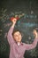 A small student launches a red airplane in the classroom against the background of a board