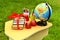 On a small student`s table against a background of green grass, there are books tied with a red gift ribbon next to a globe, multi