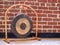 Small suspended gong sitting on wooden floor against brick wall backdrop