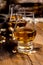 Small tasting glasses with aged Scotch whisky on old dark wooden vintage table with barley grains