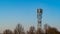 Small telecommunications tower set against a blue sky with a treeline