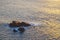Small tiny boat with breaking waves close to a small rock island at sunset, Cape Roca