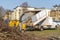 A small tipper with high sides together with a yellow wood chipper. The wood chipper shreds the branches and the wood chips are