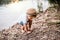 A small toddler boy standing outdoors by a river in summer, playing.