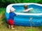 small toddler boy watches with interest at the side of the pool for his sister swimming in the water. T