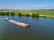 Small towboat pushes barge along calm water past fields