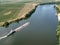 Small towboat pushes barge along calm water past fields