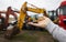 small toy excavator on a man\'s palm, in the background are real large construction excavators