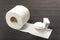 Small toy toilet bowl on roll of white toilet paper, gray background. Eco-friendly recycled toilet paper