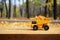 A small toy yellow truck is loaded with yellow fallen leaves. The car stands on a wooden surface against a background of a blurry