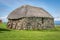 A small traditional stone built cottage with a thatched roof. a collection of metal rims for cart wheels