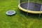 Small trampoline on big round mat, size comparison, green lawn background