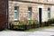 Small urban garden in front of old red brick suburban family house with dilapidated cracked facade surrounded with brown picket